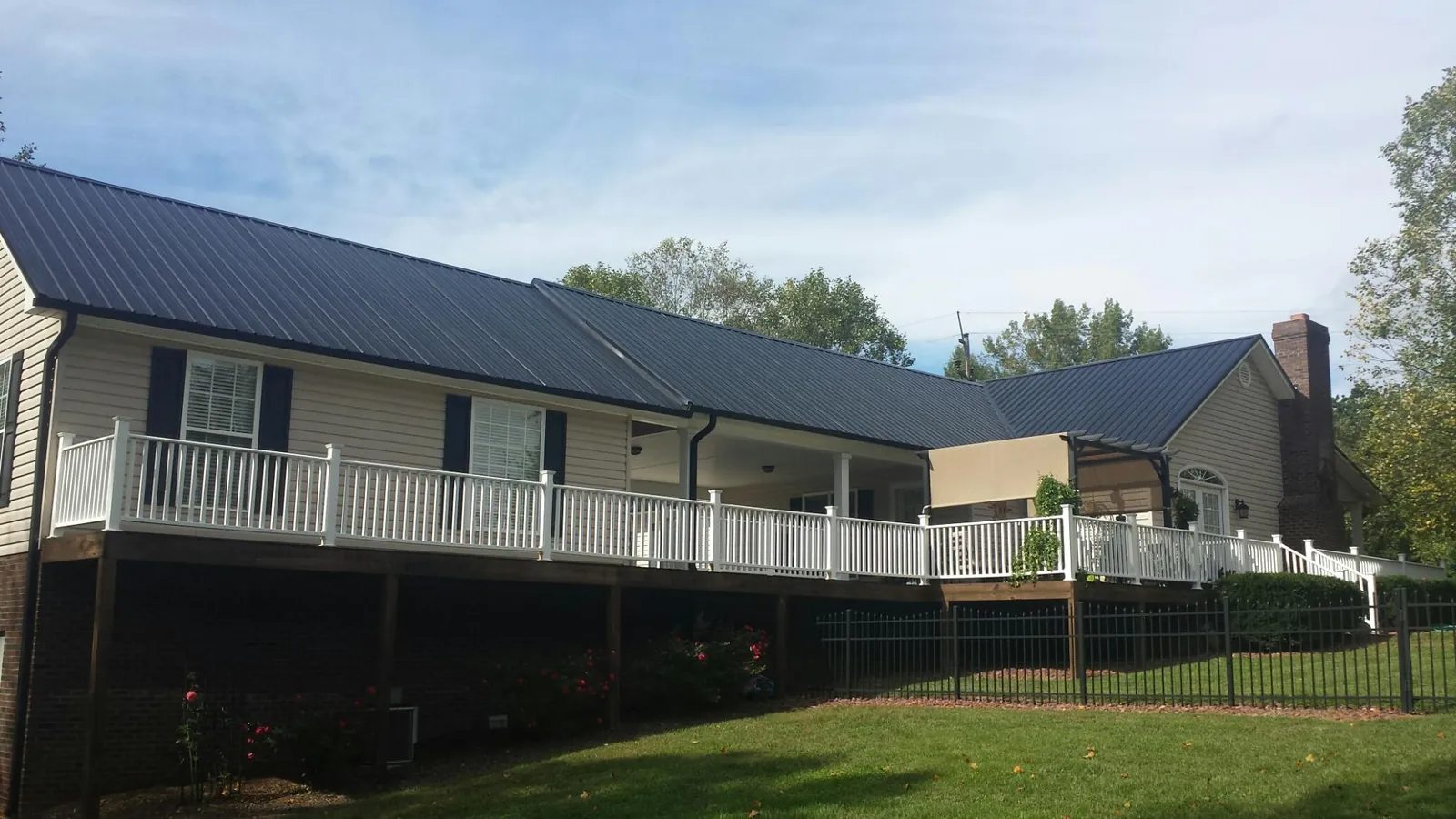 Black metal roof above a long white railed deck on a hillside home in Sylvania